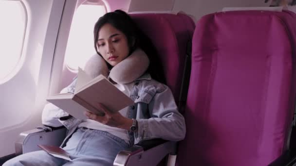 一位亚洲女性旅行者在休假期间坐飞机外出度假 一边看书一边打盹 高质量的4K镜头 — 图库视频影像