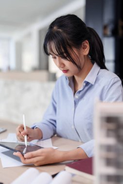 Asyalı mimar kadınlar dijital tableti çalışırken ve mimarlık planı çizerken, aynı zamanda ofiste modelleme ve inşaat mimari planıyla ilgili yeni projeler tasarlarken,.