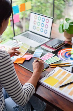 Yaratıcı grafik tasarımcısı renk seçimi için renk örneği tutuyor ve tablet üzerinde tasarım yapmak için çalışıyor.