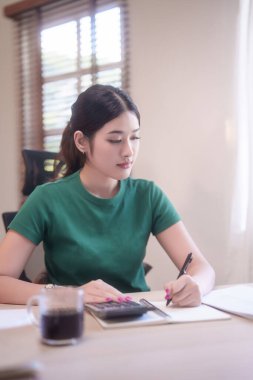 Ödev yapan Asyalı genç bayan öğrenciler ve finansman ile hesap makinesi kullanarak çevrimiçi sınıfta ders çalıştıktan sonra not defterine not alıyorlar ve evden bilgi uzaktan eğitimi alıyorlar..