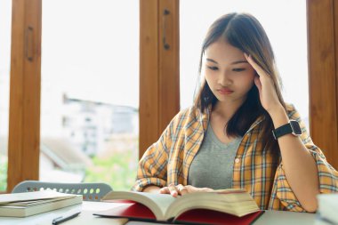 Eğitim ve okur yazarlık kavramı, üniversite öğrencisi kız kütüphanede kitap okurken kafası karışıyor.