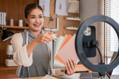 Yeni elbise koleksiyonu için renk örnekleri gösteren ve blog yazarı için video kaydeden Asyalı terzi kadınlar.