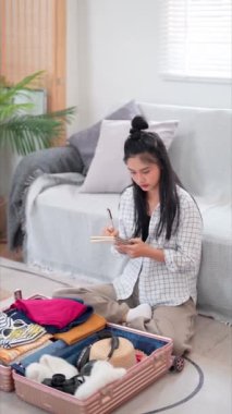 Asyalı bir kadın kontrol listesini gözden geçirmek ve hafta sonu kaçamağı için toparlanmak için bir defter kullanıyor. Uzun tatilinde rahatlatıcı bir yolculuğa hazır. Yüksek kalite 4k görüntü