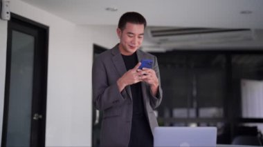 Genç Asyalı işadamı akıllı telefonundan mesaj yazıyor ya da haberleri okuyor. Yüksek kalite 4k görüntü