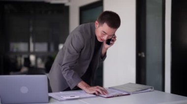 Genç Asyalı işadamı telefonda iş hakkında konuşuyor ve çalışma masasında birden fazla iş yapıyor. - Evet. Yüksek kalite 4k görüntü