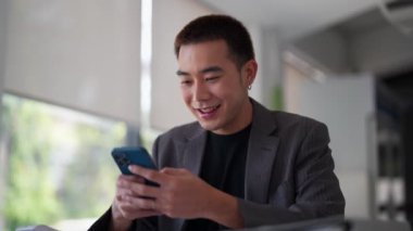 Genç Asyalı işadamı çalışma masasında mesaj yazıyor ya da akıllı telefonundan haber okuyor. - Evet. Yüksek kalite 4k görüntü