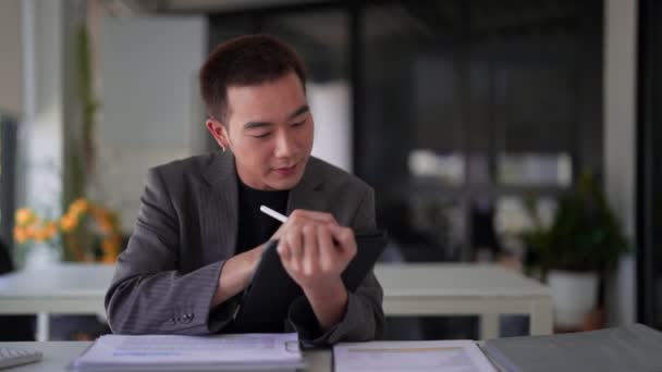 Der Junge Asiatische Geschäftsmann Schreibt Schreibtisch Arbeitsdaten Auf Sein Tablet — Stockvideo