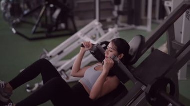 Genç Asyalı kadın spor salonunda sağlık egzersizi yapmaya tutkulu, bacak egzersizi ekipmanları kullanıyor. Formda ve aktif bir yaşam tarzı için bacak kaslarını geliştirmeye adanmıştır. Yüksek kaliteli FullHD görüntüler
