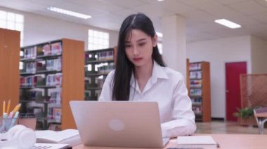 Genç Asyalı kız üniversite öğrencileri ödevlerini hararetle dizüstü bilgisayarlarında tamamlıyorlar, online iş veriyorlar, çevrimiçi derslere katılıyorlar. Yüksek kalite 4k görüntü
