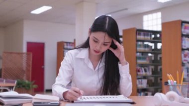Genç Asyalı kız üniversite öğrencileri öğrenim materyalleri okuyor, araştırma dersleri alıyor ve anlamakta güçlük çektikleri için üniversite kütüphanesinde hayal kırıklığına uğruyorlar. Yüksek kalite 4k görüntü
