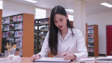 Genç Asyalı kız üniversite öğrencileri öğrenim materyalleri okuyor, araştırma dersleri alıyor ve anlamakta güçlük çektikleri için üniversite kütüphanesinde hayal kırıklığına uğruyorlar. Yüksek kalite 4k görüntü