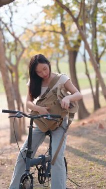 Kamu parkında bisiklet sürmeye ara verdiğinde Asyalı bir kadın sırt çantasını eşyalar için karıştırıyor. Doğanın ortasında rahat bir anın tadını çıkarıyorum. Yüksek kalite 4k görüntü