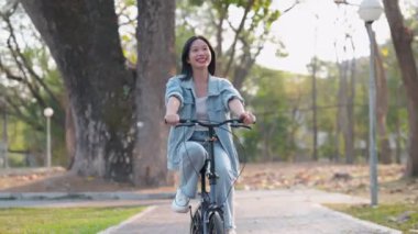 Kamu parkında bisiklet sürmekten hoşlanan Asyalı bir kadın doğanın güzelliğini kucaklıyor. Bisiklete binmek için harika bir an. - Evet. Yüksek kalite 4k görüntü