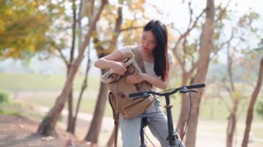 Kamu parkında bisiklet sürmeye ara verdiğinde Asyalı bir kadın sırt çantasını eşyalar için karıştırıyor. Doğanın ortasında rahat bir anın tadını çıkarıyorum. Yüksek kalite 4k görüntü