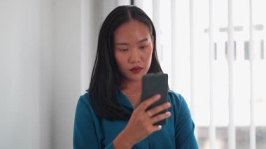 Asyalı iş kadını ofisteki son gelişmelerden haberdar olmak için akıllı telefon kullanıyor. Bilgili karar verme konusunda güncel tutuyorum. Yüksek kalite 4k görüntü