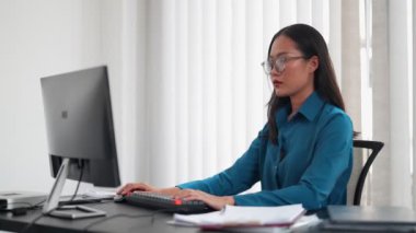 Ofisinde çalışan Asyalı iş kadını bilgisayarında yazı yazıyor. Mesleki hayatı kucaklayarak, ofis alanındaki görevlerini verimli bir şekilde tamamlıyor. Yüksek kalite 4k görüntü