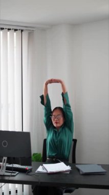 Asyalı iş kadını, iş yerinde esneyerek ve vücut egzersizleri yaparak işten kaytarıyor. Yüksek kalite 4k görüntü