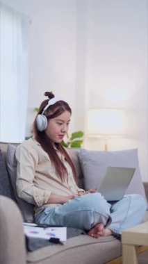 Evden çalışan Asyalı iş kadını oturma odasındaki kanepede dizüstü bilgisayarını kullanıyor. - Evet. Yüksek kalite 4k görüntü