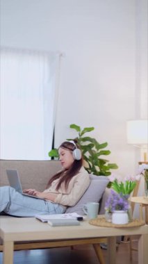 Evden çalışan Asyalı iş kadını oturma odasındaki kanepede dizüstü bilgisayarını kullanıyor. - Evet. Yüksek kalite 4k görüntü