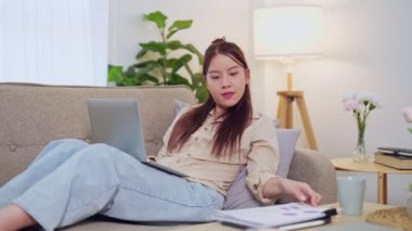 Evden çalışan Asyalı iş kadını oturma odasındaki kanepede dizüstü bilgisayarını kullanıyor. - Evet. Yüksek kalite 4k görüntü