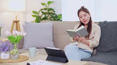 Evden çalışan Asyalı iş kadını oturma odasındaki kanepede iş defterini okuyor. Yüksek kalite 4k görüntü