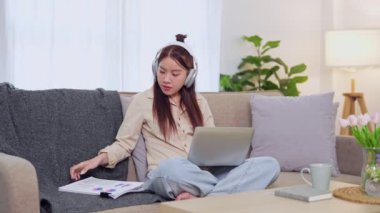 Evden çalışan Asyalı iş kadını oturma odasındaki kanepede dizüstü bilgisayarını kullanıyor. - Evet. Yüksek kalite 4k görüntü