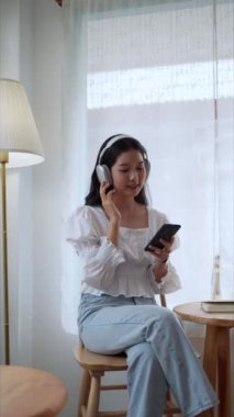 Asyalı bir girişimci, yakındaki bir kafede dinleniyor, akıllı telefonundan şarkılar seçiyor, kulaklıklarıyla müzik dinliyor, işten dinlendirici bir mola veriyor. Yüksek kalite 4k görüntü
