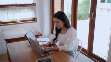 Asyalı genç bir iş kadını, yakınlardaki bir kafede laptopunu odaklanma ve kararlılıkla kullanıyor. - Evet. Yüksek kalite 4k görüntü