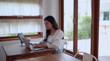 Asyalı genç bir iş kadını, yakınlardaki bir kafede laptopunu odaklanma ve kararlılıkla kullanıyor. - Evet. Yüksek kalite 4k görüntü