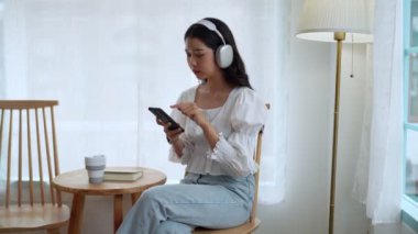 Asyalı bir girişimci, yakındaki bir kafede dinleniyor, akıllı telefonundan şarkılar seçiyor, kulaklıklarıyla müzik dinliyor, işten dinlendirici bir mola veriyor. Yüksek kalite 4k görüntü