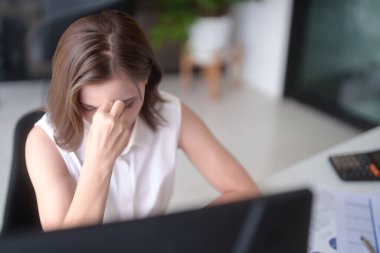 Asyalı iş kadınları yorgun ve stresli bir şekilde burunlarına masaj yaparken, yeni bir girişimin yatırım piyasası hisselerini analiz ediyor ve pazarlama raporunun planlanmasında teknolojiyi kullanıyorlar..