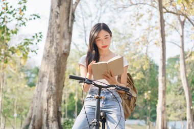 Sırt çantalı genç Asyalı kadınlar bisiklete binip mutlu bir şekilde kitap okuyorlar. Bisiklet sürdükten sonra dinleniyorlar..