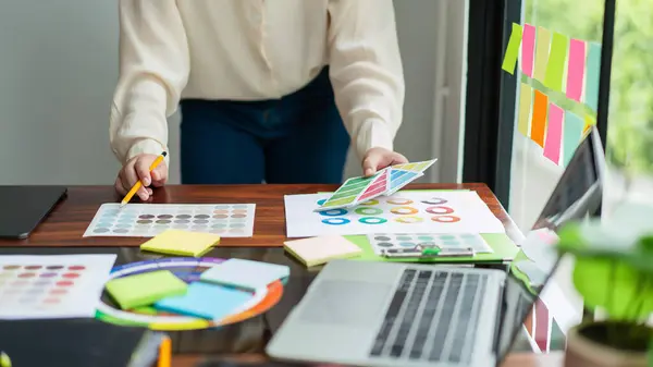 stock image Creative graphic designer holding color sample and comparing color swatch on document to designing.