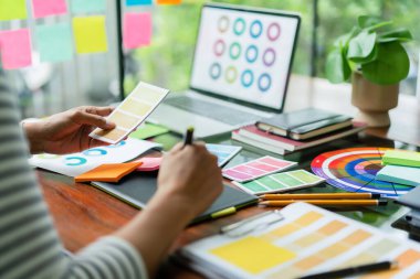 Yaratıcı grafik tasarımcısı renk seçimi için renk örneği tutuyor ve tablet üzerinde tasarım yapmak için çalışıyor.