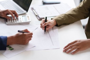 Masadaki bir belgeyi tartışan ve işaret eden iki kişinin yakın çekimi. Elleri kalemleri tutuyor, belgenin içeriğine ilişkin bir inceleme veya işbirliği gösteriyor.