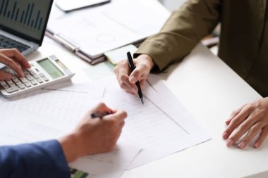 Masadaki bir belgeyi tartışan ve işaret eden iki kişinin yakın çekimi. Elleri kalemleri tutuyor, belgenin içeriğine ilişkin bir inceleme veya işbirliği gösteriyor.