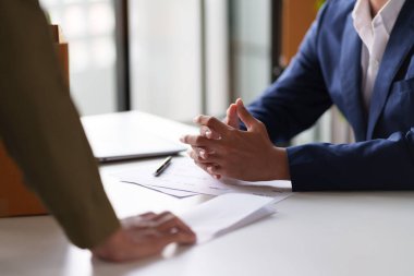 İki kişi bir masada belgeleri değiş tokuş ediyor. Bir kişi ofis malzemeleriyle dolu bir kutu tutuyor. Bu da olası bir iş değişimi ya da proje devrini gösteriyor..