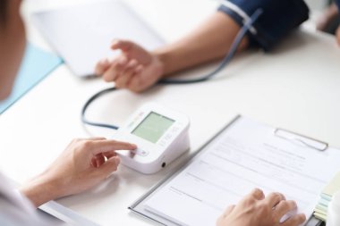 Hastanın tansiyonunu ölçen bir doktor. Hastanın kolunda tansiyon aleti var. Doktor da tansiyon monitörü kullanıyor..