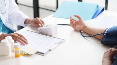 Hastanın tansiyonunu ölçen bir doktor. Hastanın kolunda tansiyon aleti var. Doktor da tansiyon monitörü kullanıyor..