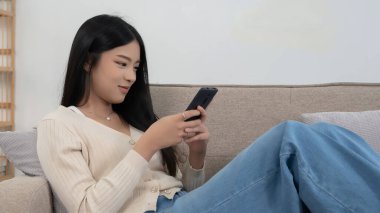 Genç Asyalı kadınlar yeni bir girişimin pazarlama verilerini okuyorlar ve akıllı telefondan mesaj yazarak sohbet ediyorlar. Bu sırada kanepede uzanıp evdeki yaşam tarzının keyfini çıkarıyorlar..