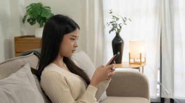 Genç Asyalı kadınlar yeni bir girişimin pazarlama verilerini okuyorlar ve akıllı telefondan mesaj yazarak sohbet ediyorlar. Bu sırada kanepede uzanıp evdeki yaşam tarzının keyfini çıkarıyorlar..