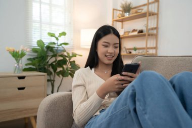 Genç Asyalı kadınlar yeni bir girişimin pazarlama verilerini okuyorlar ve akıllı telefondan mesaj yazarak sohbet ediyorlar. Bu sırada kanepede uzanıp evdeki yaşam tarzının keyfini çıkarıyorlar..