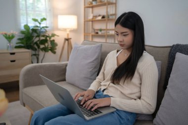 Genç Asyalı kadınlar dizüstü bilgisayarı bacaklarına takıyor ve yeni başlayanların pazarlama verilerini daktilo ederken aynı zamanda kanepede oturup evdeki yaşam tarzının keyfini çıkarıyorlar..