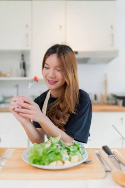 Sebzeli domates yiyen genç Asyalı kadın taze sebze salatasıyla salatayı sosla karıştırıp evde sağlıklı bir yaşam tarzıyla mutfakta sağlıklı kahvaltı hazırlıyor..