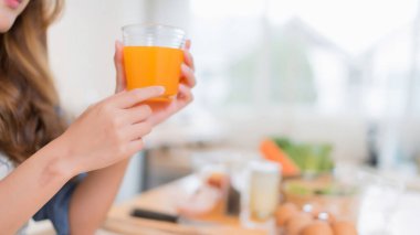 Genç Asyalı kadının elleri elinde bir bardak portakal suyu tutarken ve taze meyve içerken sebze salatası hazırlarken ve evde sağlıklı yaşam tarzıyla mutfakta sağlıklı kahvaltı hazırlarken..