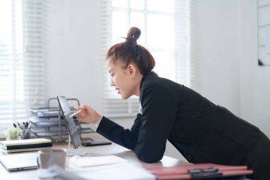 Siyah takım elbiseli bir iş kadını masasına yaslanmış modern ofis ortamındaki işine odaklanmış durumda..