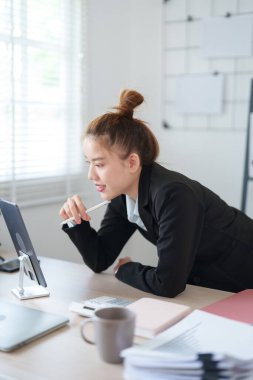 Siyah takım elbiseli bir iş kadını masasına yaslanmış modern ofis ortamındaki işine odaklanmış durumda..