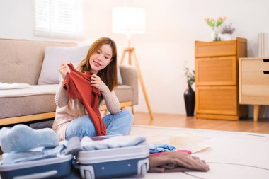 Genç bir kadın yerde oturuyor, valizini düzenlerken paketleme listesindeki eşyaları kontrol ediyor, her şeyin yolunda olduğundan emin oluyor..