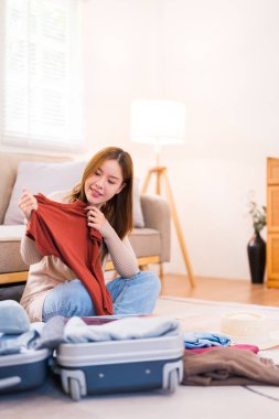 Genç bir kadın yerde oturuyor, valizini düzenlerken paketleme listesindeki eşyaları kontrol ediyor, her şeyin yolunda olduğundan emin oluyor..