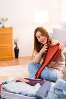 Genç bir kadın yerde oturuyor, valizini düzenlerken paketleme listesindeki eşyaları kontrol ediyor, her şeyin yolunda olduğundan emin oluyor..